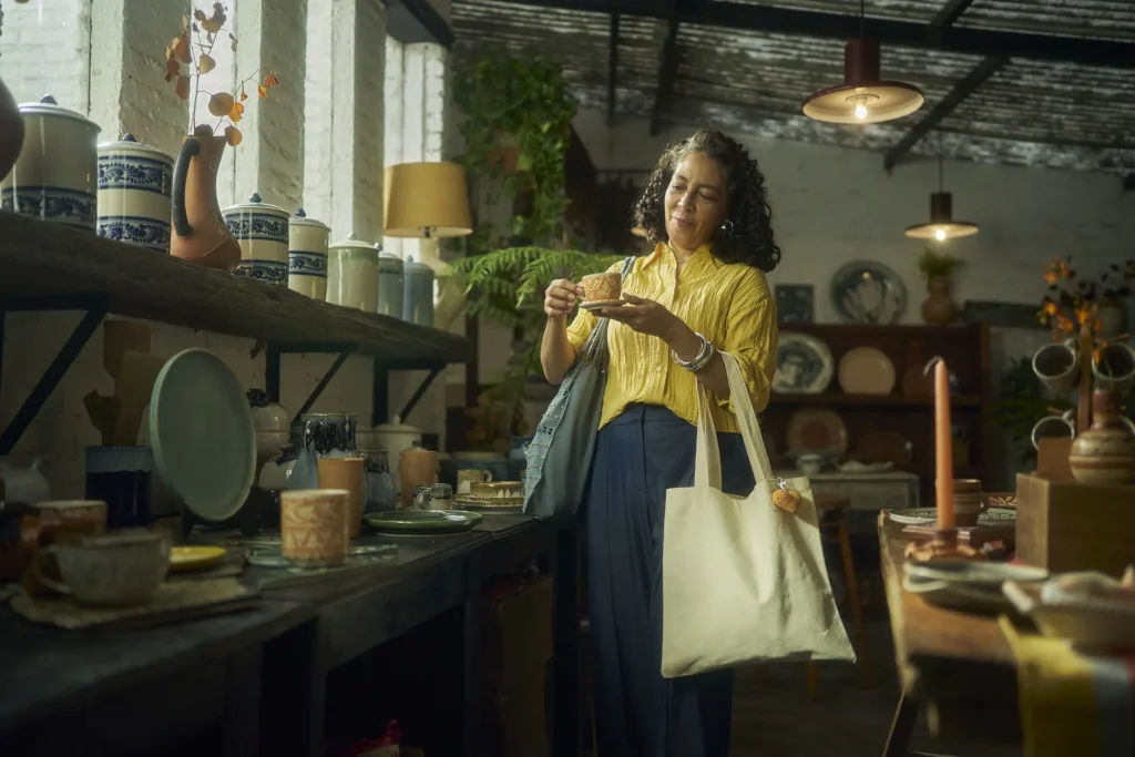 Woman holding patterned ceramic plate and canvas tote bag while shopping in pottery store with handcrafted ceramics